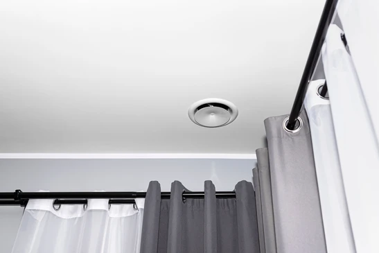 Ventilation mécanique domestique avec récupération de chaleur, un anémostat visible au plafond de la chambre, mur gris