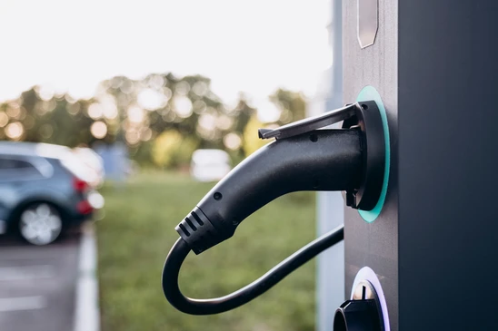 Scène extérieure avec véhicule électrique blanc en charge, câble d'alimentation jaune connecté au port de recharge latéral