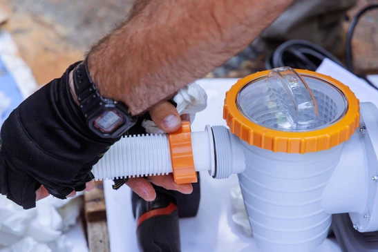 Électricien professionnel en tenue de travail effectuant le raccordement électrique d'un équipement piscine, installant un disjoncteur différentiel ou un coffret de commande étanche dans un environnement extérieur près d'une piscine résidentielle. L'image doit montrer le professionnel au travail sur une installation électrique sécurisée et normée, avec des composants visibles (câbles, boîtiers électriques) caractéristiques des installations piscine conformes aux normes.