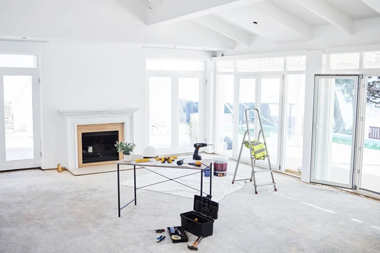 Un électricien en uniforme professionnel effectue l'installation d'une prise électrique murale dans une pièce de maison en cours de rénovation. La pièce montre des murs en préparation avec des gaines électriques apparentes, reflétant un chantier de rénovation résidentielle professionnelle. Le plan de travail est proche pour montrer la précision et le professionnalisme du geste.